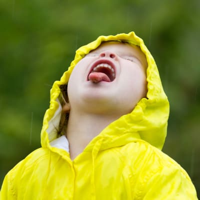 Flicka iklädd gul regnjacka räcker ut tungan och fångar regndroppar.