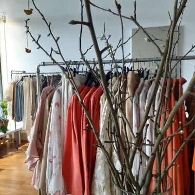 Vårkläder hänger på galgar i affär och en vas med äppelkvistar i knopp ståpr i förgrunden.