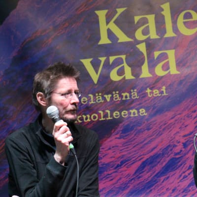 Juha Hurme ja Tuomari Nurmio puhuvat mikrofoneihin Kalevala elävänä tai kuolleena -julisteen edessä.