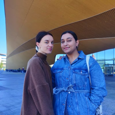Emmi Hahto och Melissa Linsa står framför centrumbiblioteket Odes orangea fasad i Helsingfors,