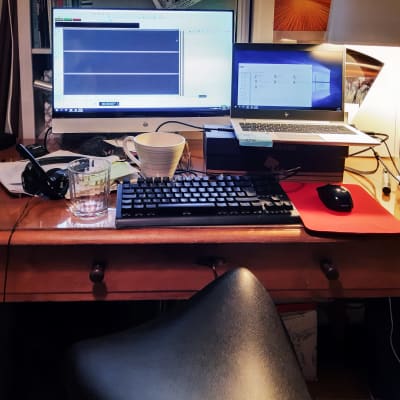 Gammalt skrivbord i trä med bärbar dator, mikrofon och hörlurar, datorskärm påslagen