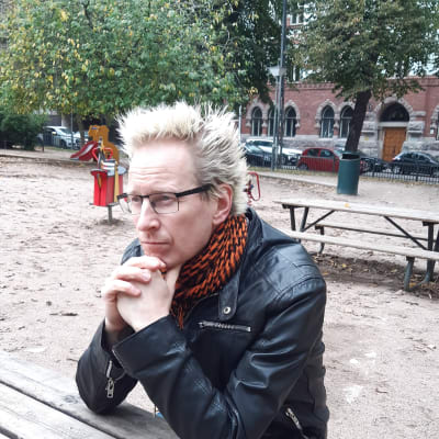 Jonas Franck sitter med hakan i händerna vid ett bord i en park och tittar rakt fram.