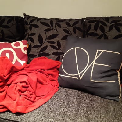 En grå soffa med en tillknycklad röd filt och en kudde med texten Love, kärlek.