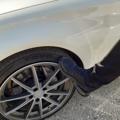 En mansfot i löparsko sparkar mot fälgen i bilens däck 
