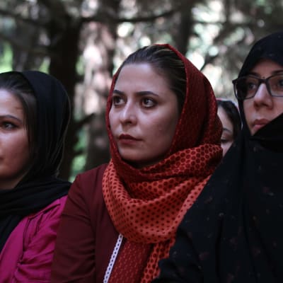 Tre afghanska kvinnor fotograferade från sidan. De tittar framåt.
