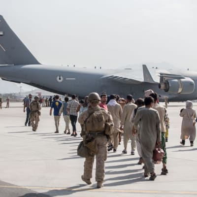 Människor på flygfältet i Kabul går mot en Air Force Boeing C-17 för att evakueras. Soldater går bredvid.
