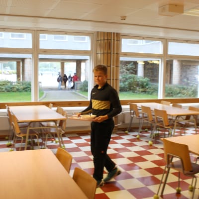pojke bär bricka i skolmatsal