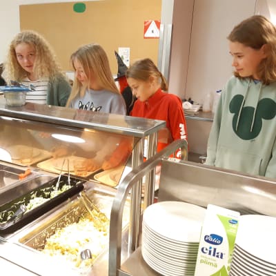 Fyra skolelever tar mat åt sig i skolans matsal.