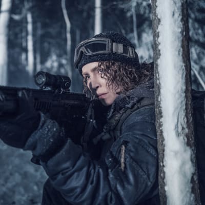 På bilden syns en kvinna som håller i ett gevär i ett vintrigt landskap.