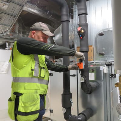En man vid en stor ventilationsanläggning. Han är klädd i gul-svarta arbetskläder med reflexer.