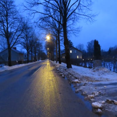 En tom, rak gata i Karis. Några gatulampor lyser. Det är tidig morgon, allt går i blått innan solen stiger upp. Vått och grått.
