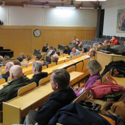 Människor sitter i ett auditorium. Fotograferat så att man ser mest ryggar.