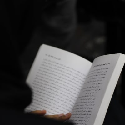 Nainen pitää käsissään kirjaa, jossa on farsinkielistä tekstiä.