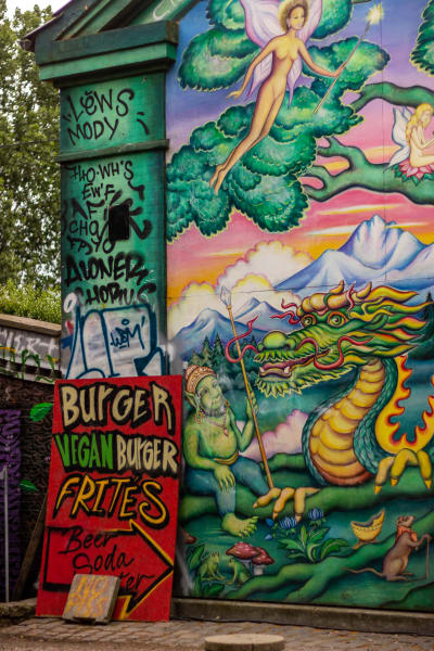 En målad vägg med sagokaraktärer. Framför väggen står en skylt som gör reklam för veganska hamburgare.
