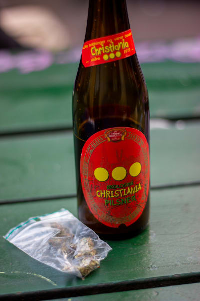 En ölflaska med Christiania-etikett och en minigrippåse med cannabis på ett bord.