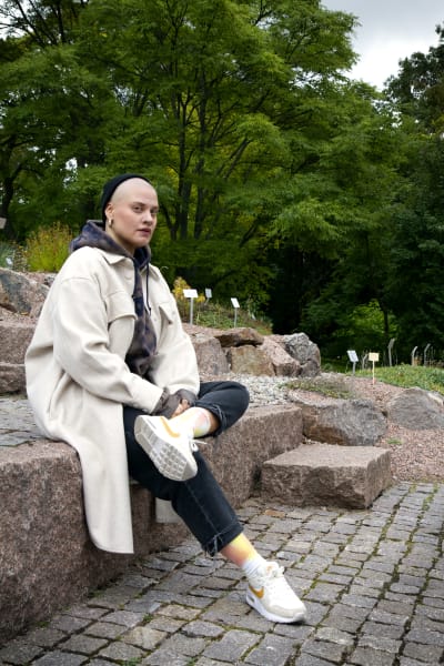 Katja Maria / Kay Taavitsainen istuu kiviportaikolla toinen jalka polven päällä.