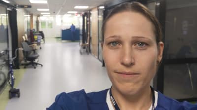 En kvinna i sjuksköterskekläder sitter i en korridor på ett sjukhus.