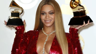 Artisten Beyoncé iklädd röd klänning håller upp två Grammy-pris.