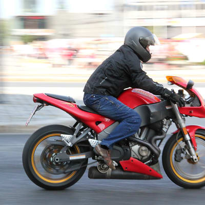 En människa som åker på en röd motorcykel. Personen är svarklädd med svart hjälm på huvudet.