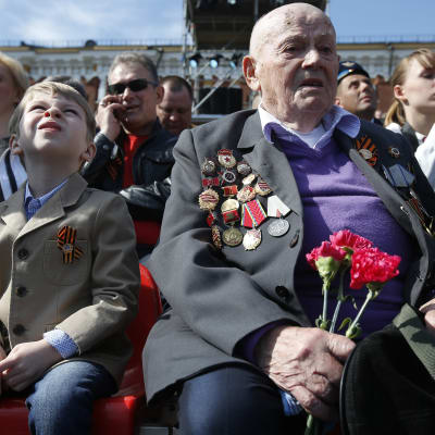En krigsveteran och andra ryssar sitter på Röda torget den 9 maj 2015 i väntan på att segerdagsparaden ska inledas.