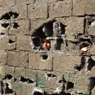 Kurdiska pojke tittar ut genom sönderskjuten mur i Cizre