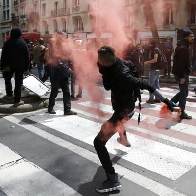 En maskerad demonstrant i Paris slänger tillbaka en tårgaskanister som polisen har avfyrat mot demonsranter