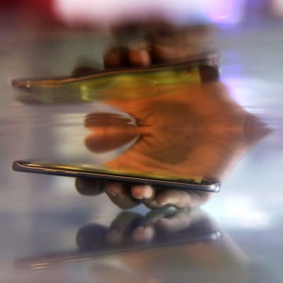 En hand sticker ner en smarttelefon i vatten och en suddig eterisk spegling av handen och telefonen syns i ytan ovanför.