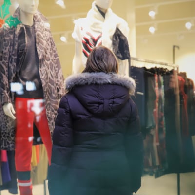 En person i vinterjacka tittar in genom ett skyltfönster till en klädbutik.