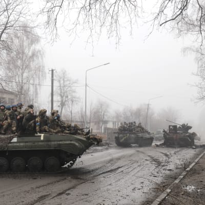 Ukrainska soldater, iklädda kamouflageuniform och blåa hjälmar, sitter på pansarvagnar omgivna av dimma.