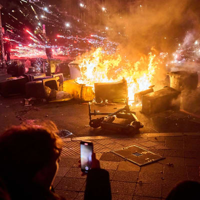 Nuoret pystyttivät palavan barrikadin Sanderstraßen ja Kottbusser Dammin risteykseen Berliinin Neuköllnin kaupunginosassa uudenvuodenyönä 2023. Ihmiset kuvaavat palavaa barrikadia.