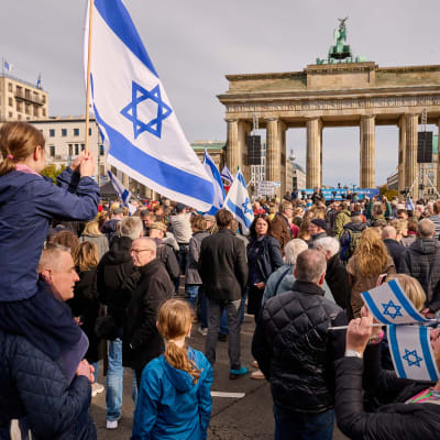 En folkmassa vid Brandenburger Tor i Berlin i Tyskland. Ett barn sitter på en vuxen persons axlar och håller i en israelisk flagga.