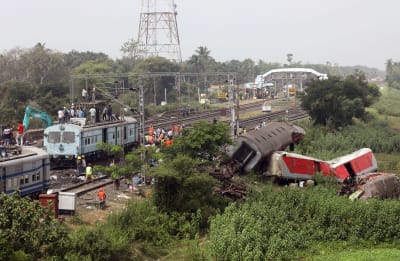 Trasiga järnvägsvagnar ligger bredvid rälsen i Balasore i Indien. Järnvägsarbetare arbetar med rälsen.