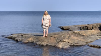 En kvinna i sommarklänning står på klipporna ute vid havskanten.