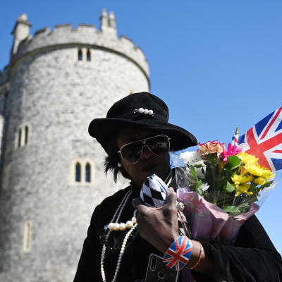 En person med solglasögon bär på en brittisk flagga och gula och rosa blommor.