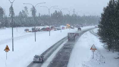 Krockade bilar, en ambulans och bärgningsfordon syns på en snöig landsvägssträcka.