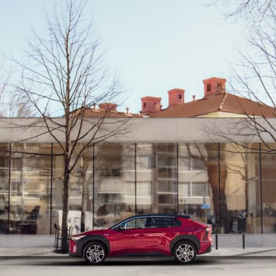 En röd elbil är parkerad framför Åbo stadsbibliotek med sina stora glasfönster.