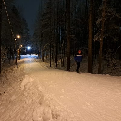 Hiihtäjä hiihtää ensilumen latua Turun Impivaarassa illan pimeydessä.