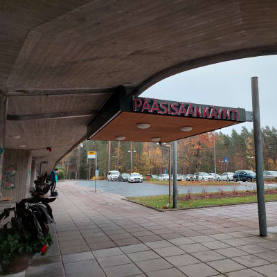 Sairaalan pääsisäänkäynnin ovella on pyöriä ja parkkipaikalla autoja.