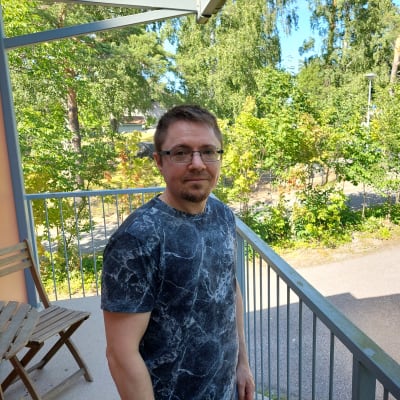 Maskinmontör och musiker Jens Lindqvist poserar på en balkong med träd i bakgrunden.