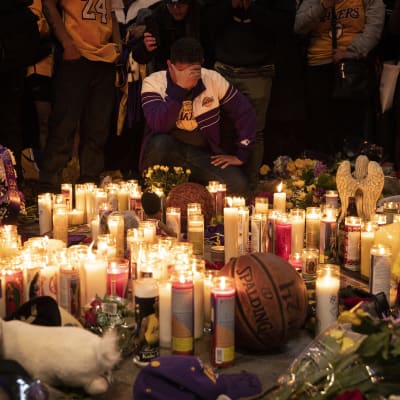 Person håller sig för ansiktet framför tända ljus för att hedra Kobe Bryant.