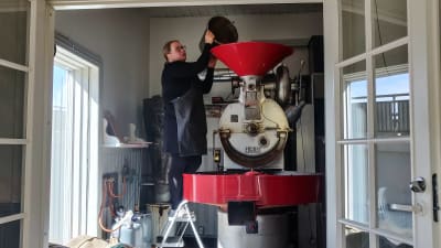 En kvinna häller bönor i en kafferost.