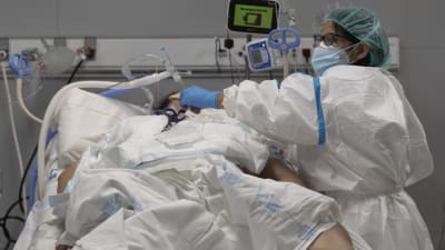 En vårdare i skyddsutrustning står vid en sjukhussäng med en patient på IVA i ett sjukhus i Madrid.