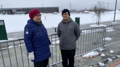 Två personer står framför ett stängsel, i bakgrunden Torneå-Haoaranda resecentrum