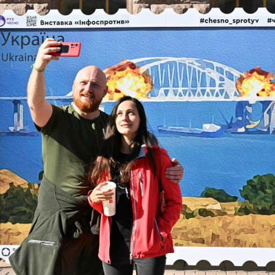 Pariskunta kuvaa itseään suuren postimerkin edessä. 