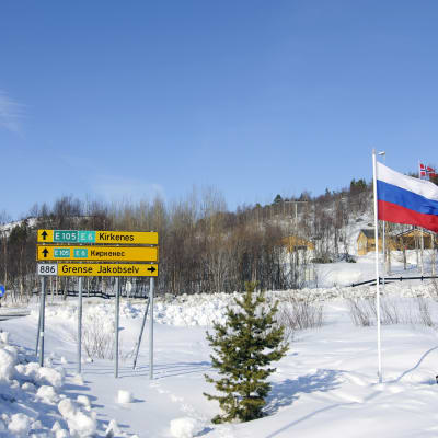 Vägskyltar på norska och ryska i Kirkenes. Intill skyltarna i det snöiga landskapet vajar en rysk och en norsk flagga.