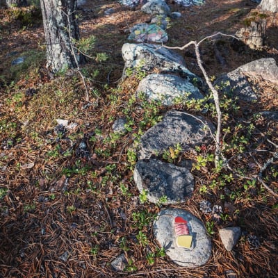 Värikkäitä mosaaikinpaloja kiinnitettynä kiviin metsässä