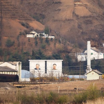 Pohjois-Korean ja Kiinan välinen raja. Korean puolella näkyy valtavan kokoiset kuvat maan entisistä johtajista.