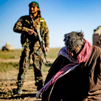 Tillfångagna misstänkta IS-medlemmar bevakas av en SDF-soldat