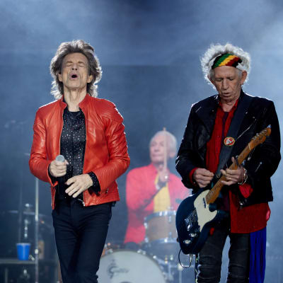 På bilden syns bandet Rolling Stones uppträda under en konsert i Berlin år 2018. I mitten står sångaren Mick Jagger klädd i en röd läderjacka.