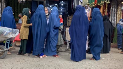 Sex kvinnor köper burkor på en marknad i Kabul i Afghanistan. En man står framför dem. Bilden är från den 10 maj 2022.